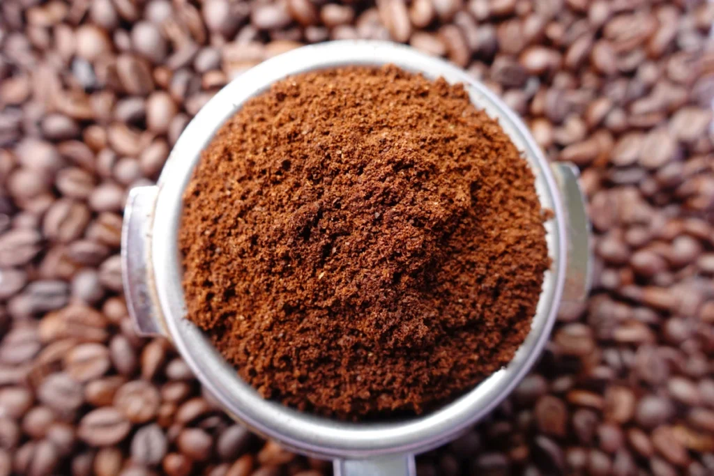 A portafilter filled with freshly ground coffee sits on a bed of whole coffee beans.