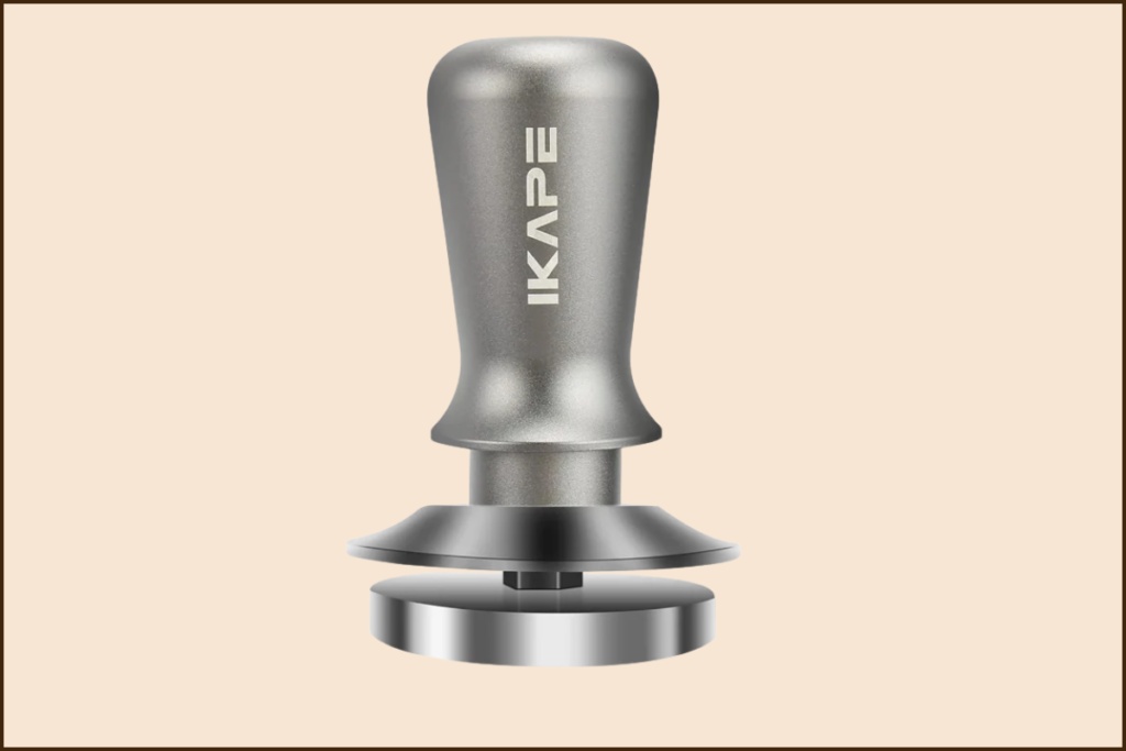 A metal coffee tamper with a cylindrical handle labeled "IKAPE" on a light beige background.