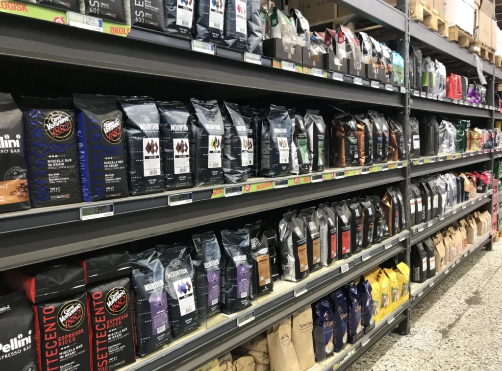 Shelves in a store displaying a variety of packaged coffee bags, arranged in rows by brand and type.
