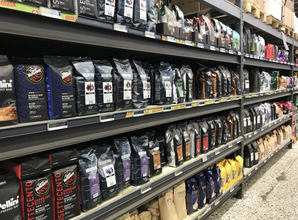 Shelves in a store displaying a variety of packaged coffee bags, arranged in rows by brand and type. Shelves in a store displaying a variety of packaged coffee bags, arranged in rows by brand and type.